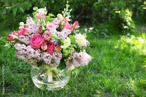 Vase with beautiful blooming bouquet of flowers on grass in garden
