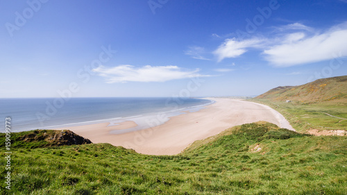 Rhossili bay sandy beach on a sunny cloudy day summer time green vegetation in south wales