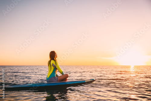Young girl on stand up paddle board on a quiet sea with warm summer sunset colors. Relaxing on ocean