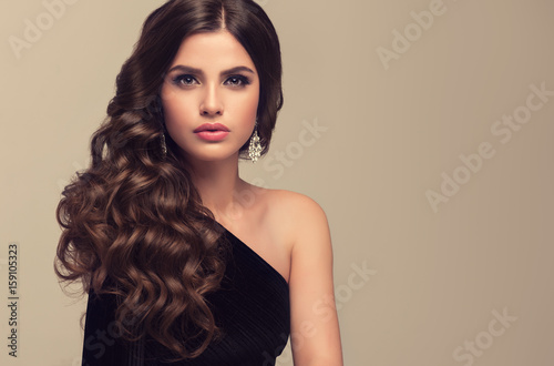 Brunette girl with long and shiny wavy hair . Beautiful model with curly hairstyle .
