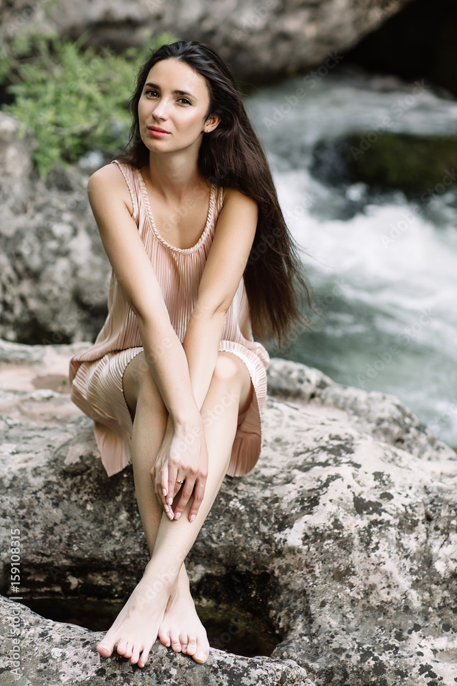 Beautiful brunette sitting on a rock in the middle of the river, water, waterfall. Beautiful nature, natural light, soft, filling Beautiful brunette sitting on a rock in the middle of the river, water, waterfall. Beautiful nature, natural light, soft, filling