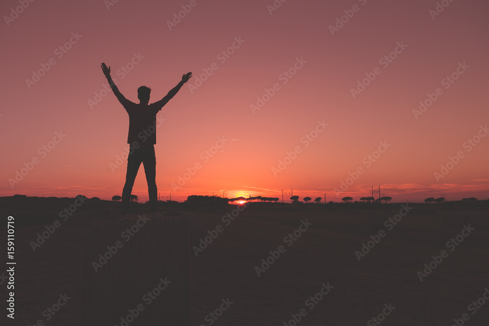 Ragazzo su una balla di fieno con le mani a v di fronte al tramonto