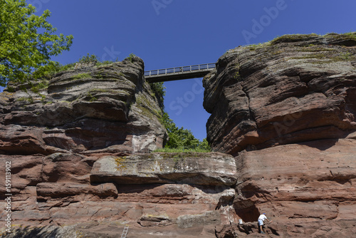 Man cleaning the red rocks below a bridge that connects the red ruins of the decayed castle Haut-Barr, Saverne, France