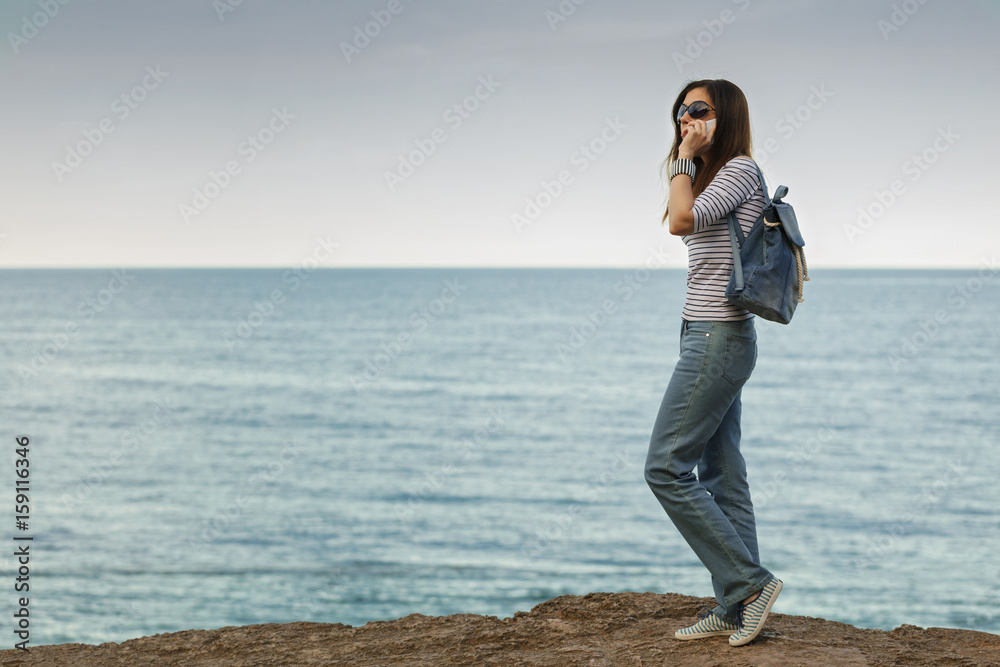 Young woman in jeans, in striped top and sneakers on the beach by the sea. Young woman in jeans, in striped top and sneakers on the beach by the sea.