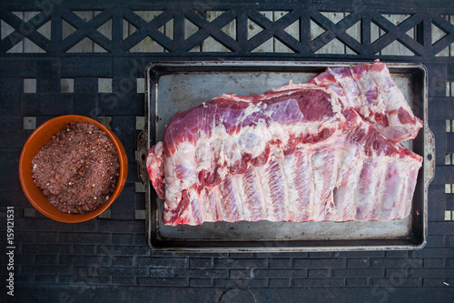 Pork rack of baby back ribs with bowl of dry spice rub ready for summer grill