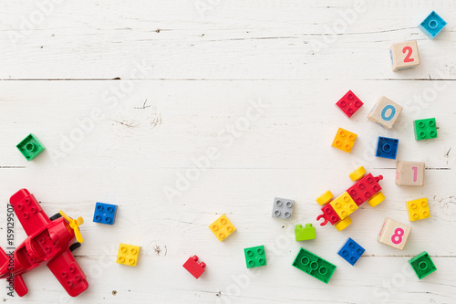 Top view on wooden cubes with numbers and colorful toy bricks and  plane on white wooden background. Toys in the table photo