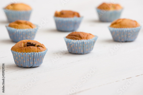 Closeup of homemade vanilla muffins in blue paper cups on white wooden background. Healthy snack.