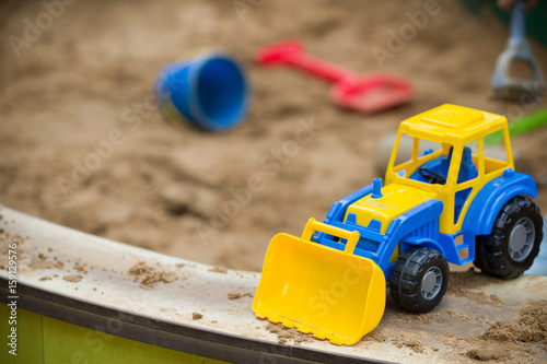 Closeup of bright blue and yellow tractor and children plastic shovel and pail in the sandbox. Baby's toys outdoor. © goodmoments