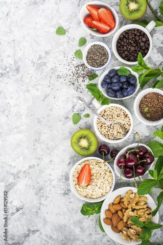 Healthy fitness food from fresh fruits  berries  greens  super food  kinoa  chia seeds  flax seed  strawberry  blueberry  kiwi  cherry  almonds  walnuts  mint  oatmeal natural flakes on a light marble