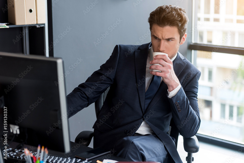 Fototapeta premium Young man is sitting at his desk with beverage