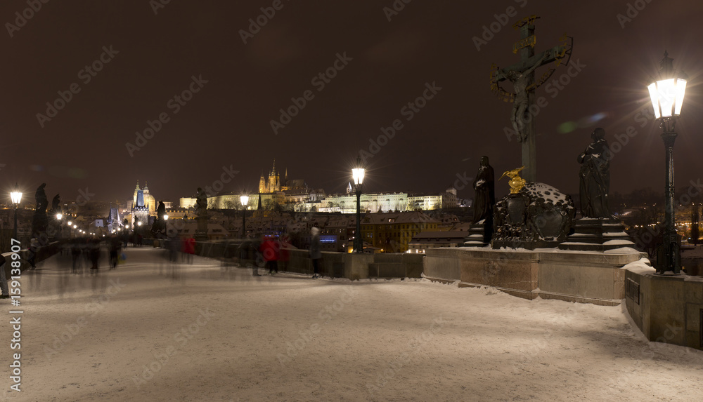 Night snowy Prague Lesser Town with gothic Castle, Bridge Tower and St. Nicholas' Cathedral from Charles Bridge with its baroque Statues, Czech republic