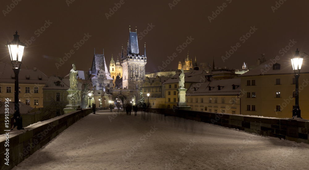 Obraz premium Night snowy Prague Lesser Town with gothic Castle, Bridge Tower and St. Nicholas' Cathedral from Charles Bridge with its baroque Statues, Czech republic