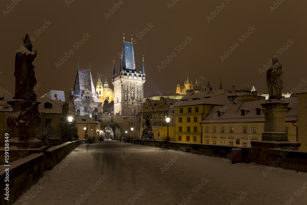 Obraz premium Night snowy Prague Lesser Town with gothic Castle, Bridge Tower and St. Nicholas' Cathedral from Charles Bridge with its baroque Statues, Czech republic