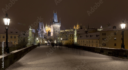 Night snowy Prague Lesser Town with gothic Castle, Bridge Tower and St. Nicholas' Cathedral from Charles Bridge with its baroque Statues, Czech republic © Kajano