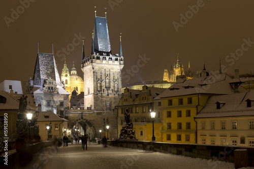 Night snowy Prague Lesser Town with gothic Castle, Bridge Tower and St. Nicholas' Cathedral from Charles Bridge with its baroque Statues, Czech republic