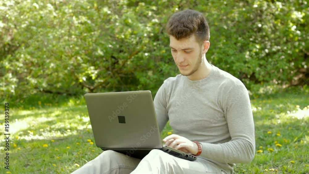 thoughtful young guy writes on a laptop in the Park thoughtful young guy writes on a laptop in the Park