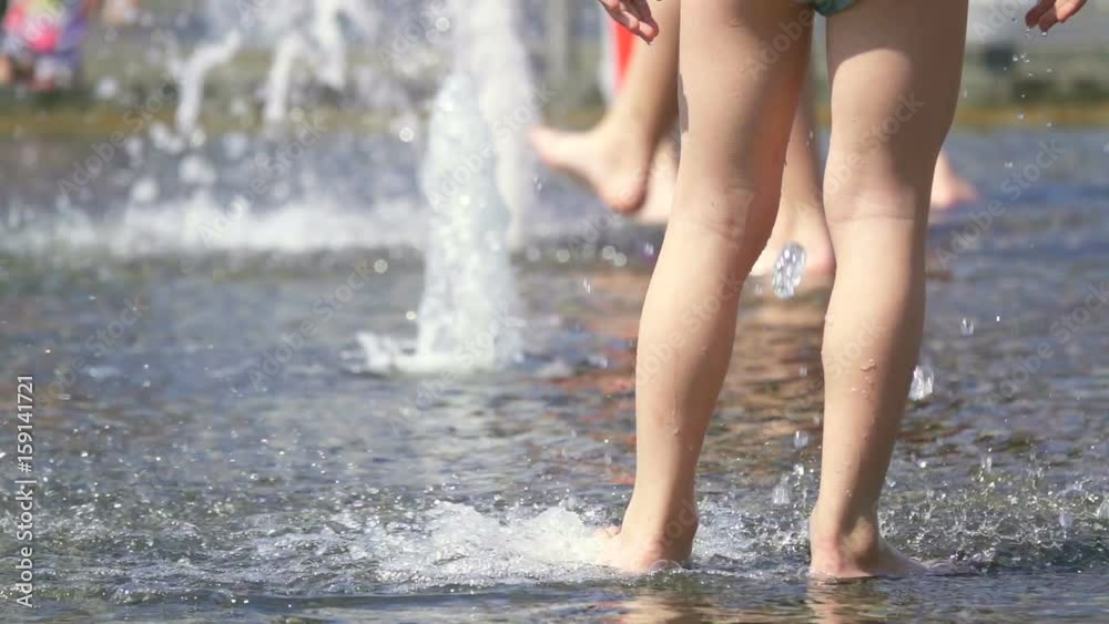 Rear view of a little boy playing in a fountain substituting his leg under a stream, slow motion Rear view of a little boy playing in a fountain substituting his leg under a stream, slow motion