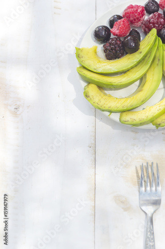 Healthy breakfast ingredients avocado slices with mix berries and honey.