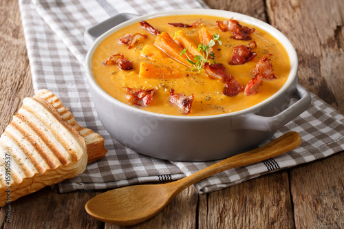 Sweet potato soup with bacon and herbs in a pan and toast close-up. horizontal