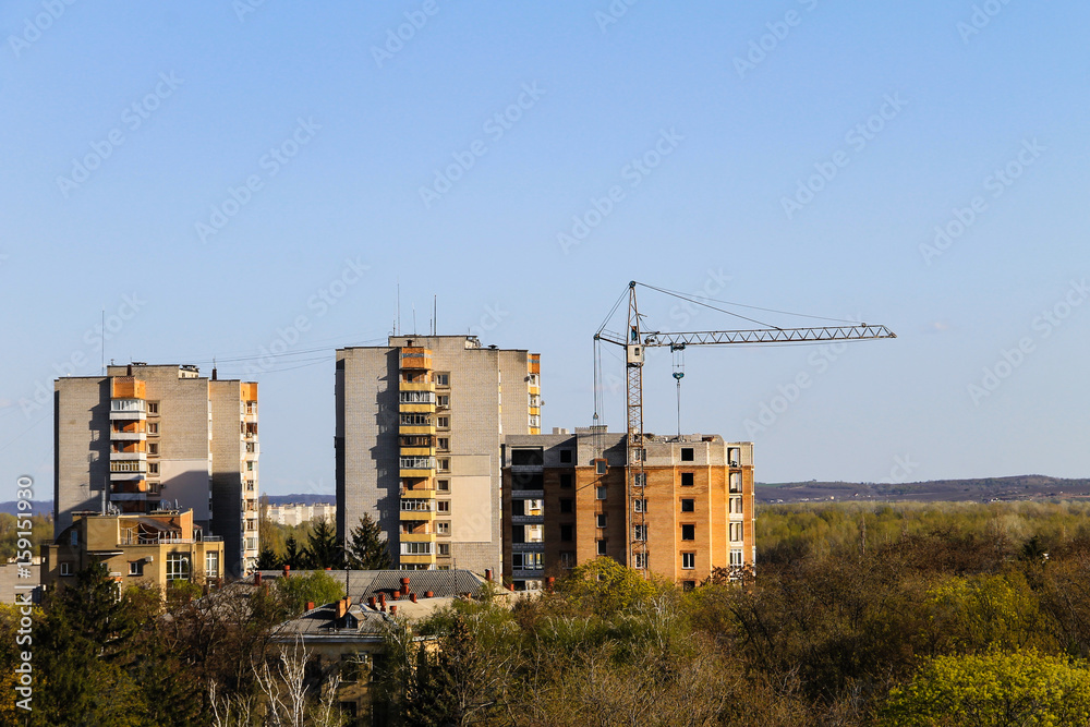 Fototapeta premium Building crane and building under construction against blue sky
