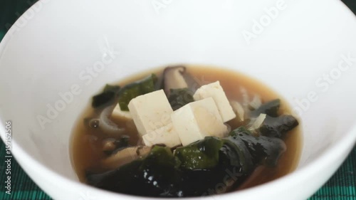 Close up of japanese miso soup poured into white bowl. It is traditional japanese food usually made of tofu, shiitake mushrooms, wakame seaweed and miso paste and is often eaten for breakfast.