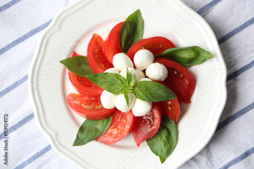 CAPRESE SALAD WITH TOMATOES, MOZZARELLA CHEESE AND BASIL LEAF ON A WHITE PLATE.