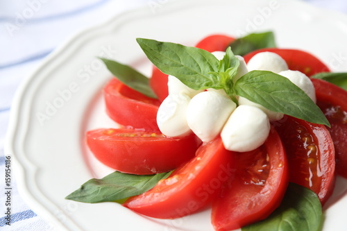 CAPRESE SALAD WITH TOMATOES, MOZZARELLA CHEESE AND BASIL LEAF ON A WHITE PLATE.