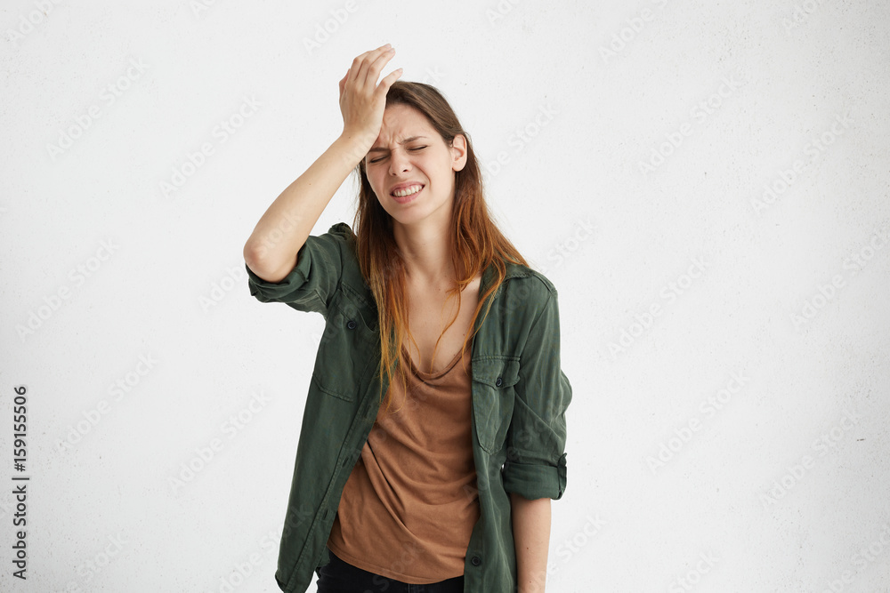 Frustrated brunette woman wearing casual clothes holding hand on forehead being depressed regreting what she done having headache. Confused female with frowned face looking stressful having some pain Frustrated brunette woman wearing casual clothes holding hand on forehead being depressed regreting what she done having headache. Confused female with frowned face looking stressful having some pain