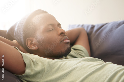 Foto Sleeping handsome black man with full lips wearing black hat and green T-shirt having good dreames being tired after work