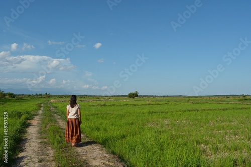 The girl stands on the ground in the field, looking at the waterless field behind the blue sky.