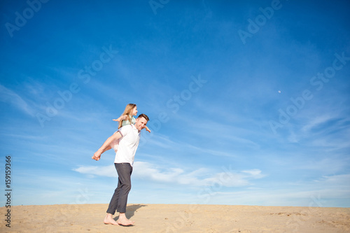 Dad and little girl daughter playing on the beach, fly, run, laugh at the blue sky background