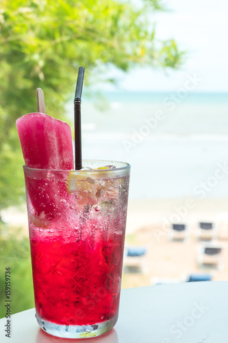 Red drink mixed soda with ice cream and lemon on blurred beach background