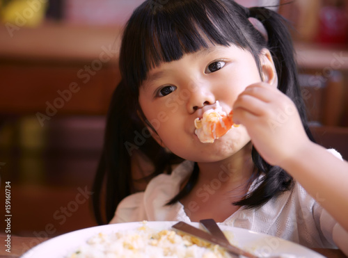 Asian children cute or kid girl eating shrimp or shrimp fried rice delicious food on table and white dish for lunch in the restaurant
