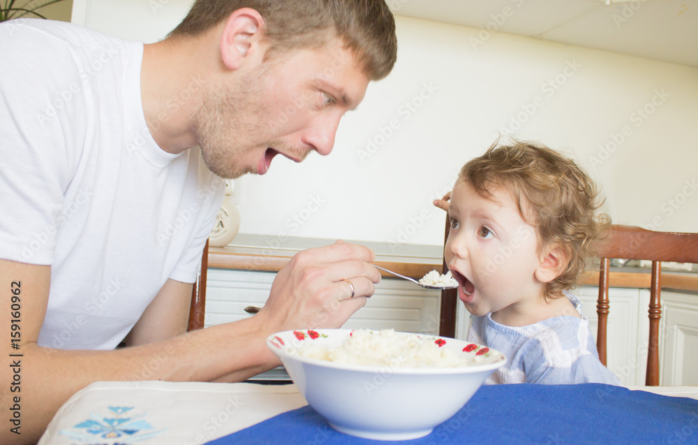 Dad feeds the baby porridge. The child does not want to eat porridge. Young father Dad feeds the baby porridge. The child does not want to eat porridge. Young father