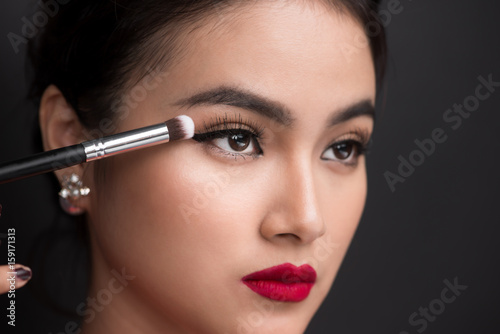 Close up of hand of asian woman applying eyeshadow on female eyelid.