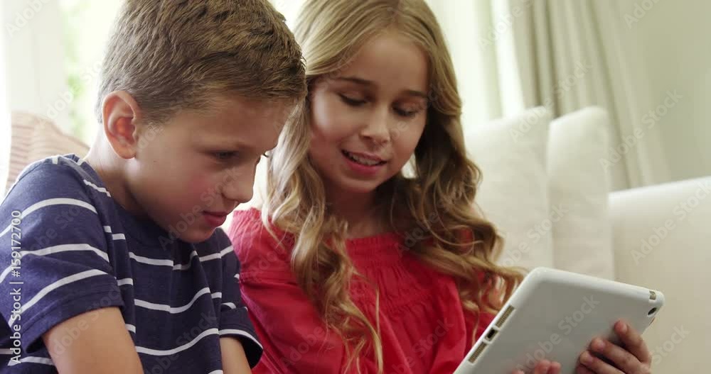 Siblings using digital tablet in living room Siblings using digital tablet in living room