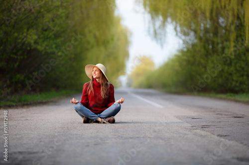 Cute healthy girl in a straw hat sitting in the lotus of the asphalt road, looking at the camera