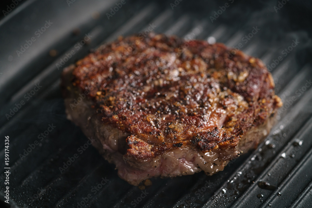beef rib eye steak on grill pan closeup, shallow focus