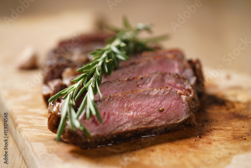 sliced medium rib eye steak with rosemary branch, closeup photo