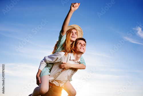 Young man piggybacking his happy girlfriend with raised hand. Cheerful lovers dreaming.