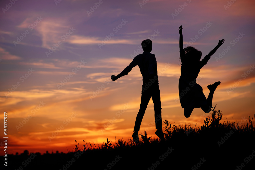 A young man with his girlfriend jump on background sunset silhouette A young man with his girlfriend jump on background sunset silhouette
