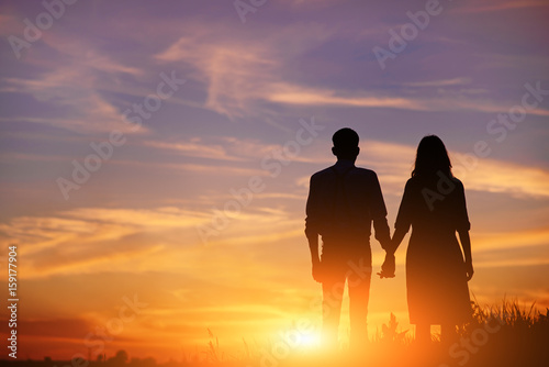 Obraz na płótnie young couple is holding hands on a background sunset silhouette w salonie
