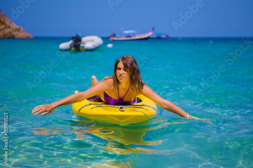 Young tanned woman lies on a yellow SUP surfboard. She swims on the waves in the ocean serenely. Relax to get away from problems. Concept