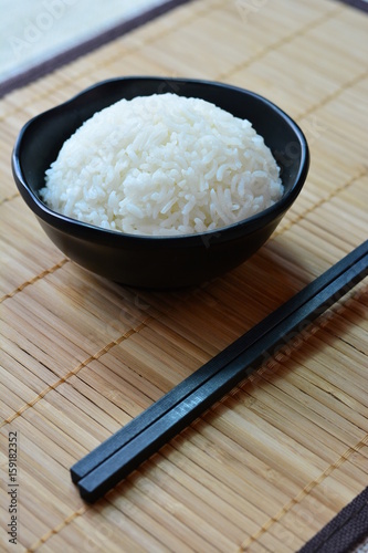 Rice in a black bowl on a bamboo mat and chopsticks