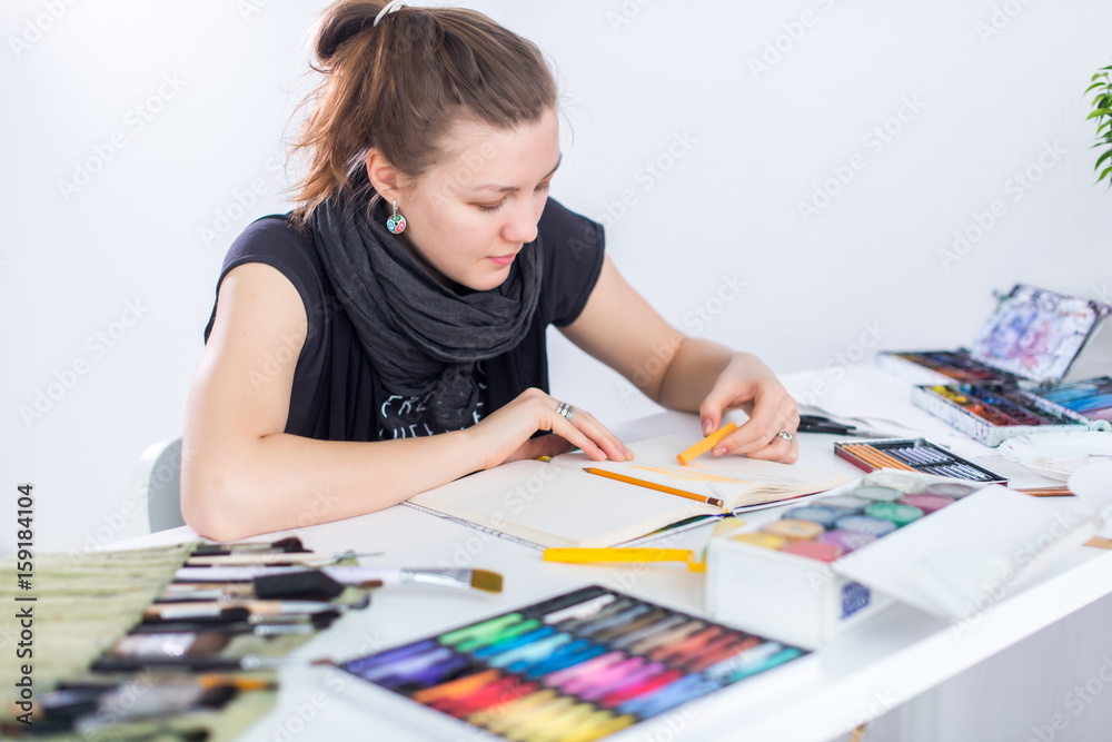 Young female artist drawing sketch using sketchbook with pencil at her workplace in studio. Side view portrait of inspired painter. Young female artist drawing sketch using sketchbook with pencil at her workplace in studio. Side view portrait of inspired painter.