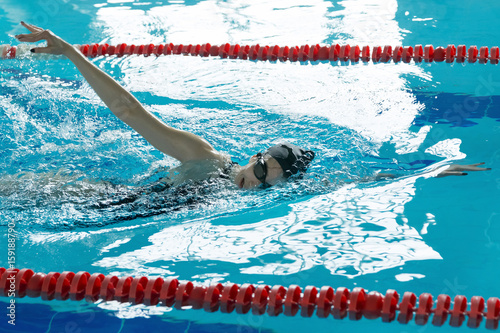 Young girl in goggles and cap swimming crawl stroke style in the blue water pool.