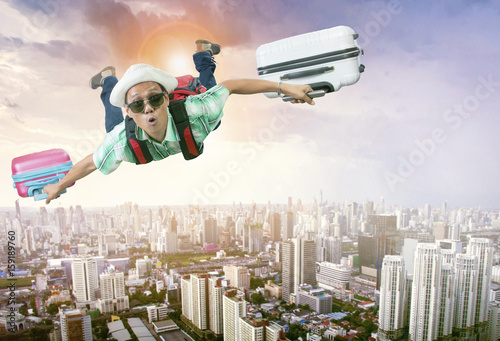 happiness face of asian traveling man flying with two luggage bag floating mid air over town skyscraper photo