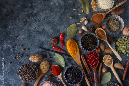 Various indian spices in wooden spoons and metal bowls, herbs and nuts on dark stone table. Colorful spices, top view,space for text. Healthy food background