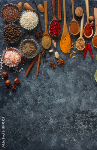Fototapeta Naklejka Na Ścianę i Meble -  Various indian spices in wooden spoons and metal bowls, herbs and nuts on dark stone table. Colorful spices, top view,space for text. Healthy food background