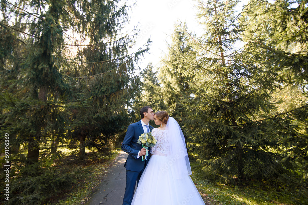 Wedding couple in love. Beautiful bride in white dress with brides bouquet and handsome groom in blue suite standing and embracing each other Wedding couple in love. Beautiful bride in white dress with brides bouquet and handsome groom in blue suite standing and embracing each other